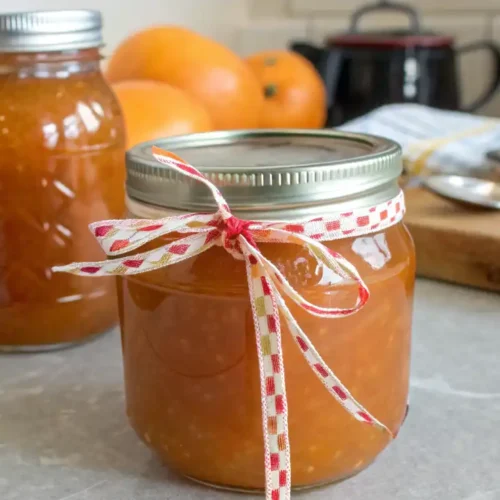 Homemade persimmon jelly in jars with fresh persimmons and ingredients.