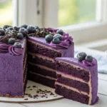 A luxurious four-layer purple velvet cake with piped frosting swirls and sugared blueberries, featuring a slice removed to reveal the moist interior.